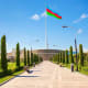 Azerbaijan flag flying on a tall flagpole in a public plaza with cypress trees and modern architecture in the background